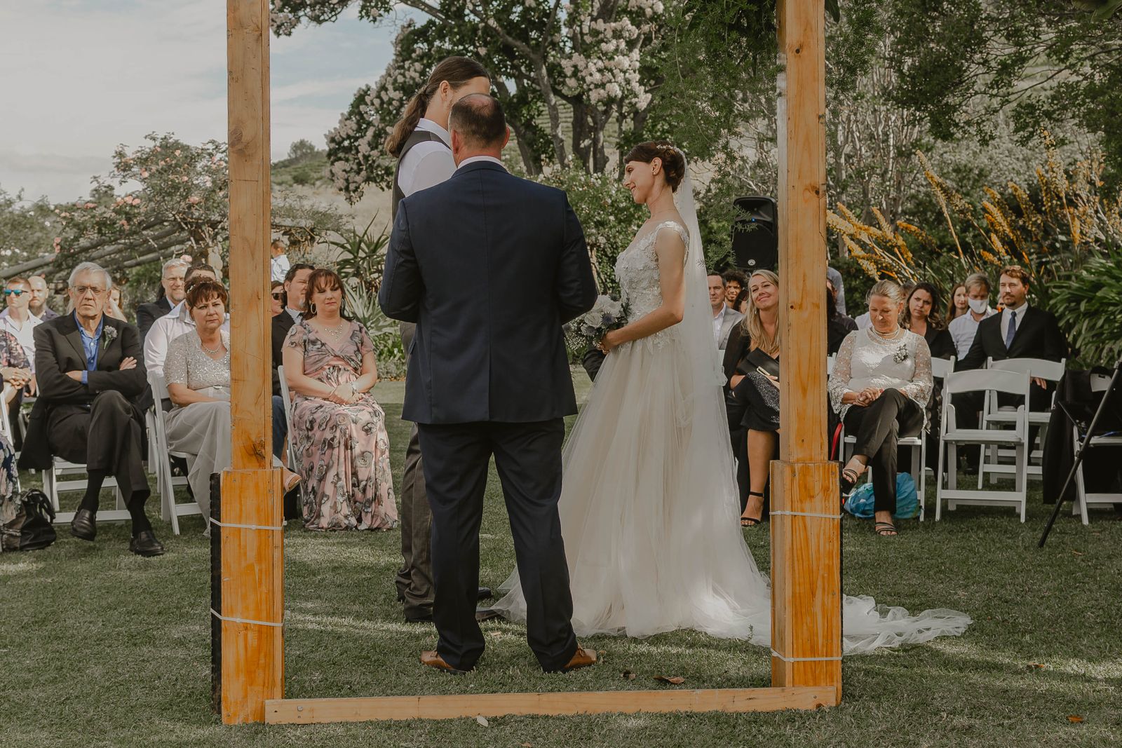 Officiant leading an outdoor wedding ceremony beneath a wooden arch